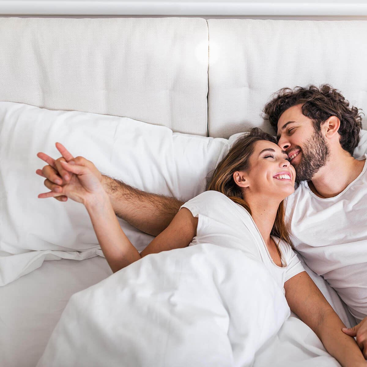 Couple smiling and relaxing in bed with white bedding.