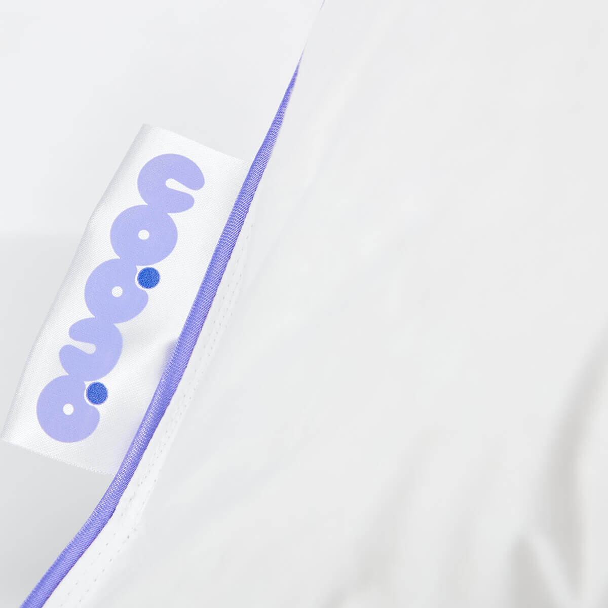 Close-up of Daunenkissen Nordic.Trio pillow edge with QUQON logo and purple trim, highlighting quality craftsmanship.